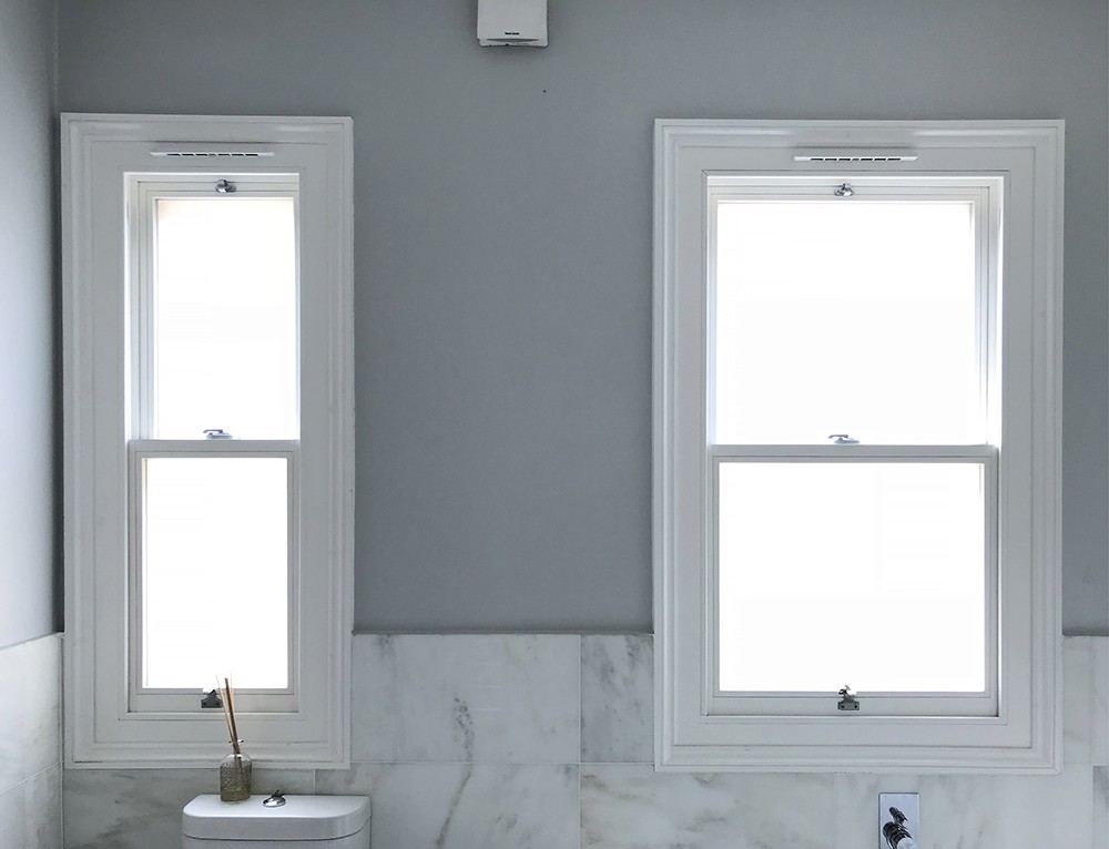 Two white timber box sash windows in a marble bathroom